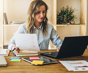 Young businesswoman woman is sitting at kitchen table and uses laptop, working, studying. On table tablet computer, paper documents. Freelancer works at home. Online marketing, education, e-learning.